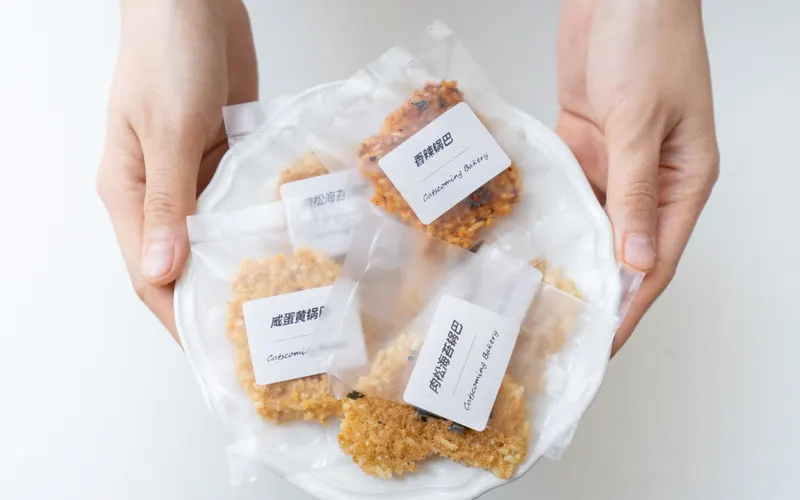 Hands holding a plate of individually bagged cookies, each bag with a printed white front label