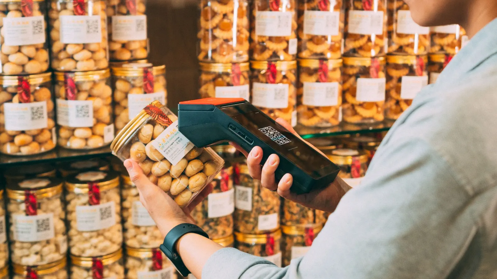 Hand scanning the label on a jar with a handheld scanner in front of shelves of labeled jars